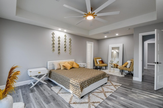 bedroom featuring a tray ceiling, wood finished floors, recessed lighting, and baseboards