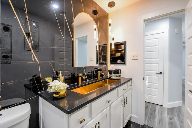 bathroom with toilet, vanity, wood finished floors, and baseboards