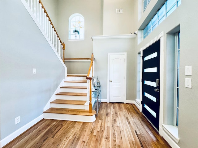 foyer entrance featuring a towering ceiling, stairs, wood finished floors, and baseboards
