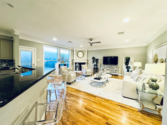 living area featuring light wood-style floors, ceiling fan, ornamental molding, recessed lighting, and a fireplace