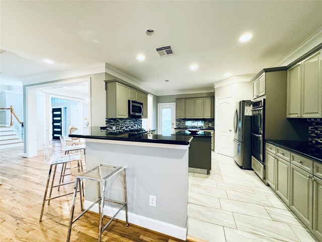 kitchen featuring crown molding, dark countertops, stainless steel appliances, tasteful backsplash, and a kitchen bar