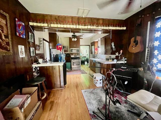 1227 W 25th St, Houston, TX 77008 - kitchen featuring stainless steel appliances, ceiling fan, light countertops, light wood-type flooring, and wood walls
