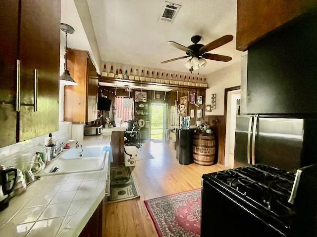 1227 W 25th St, Houston, TX 77008 - kitchen with tile countertops, a sink, ceiling fan, black gas stove, and wood finished floors