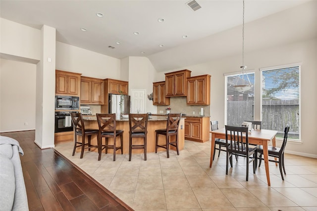 kitchen with black appliances, brown cabinetry, light stone counters, a kitchen island, and recessed lighting