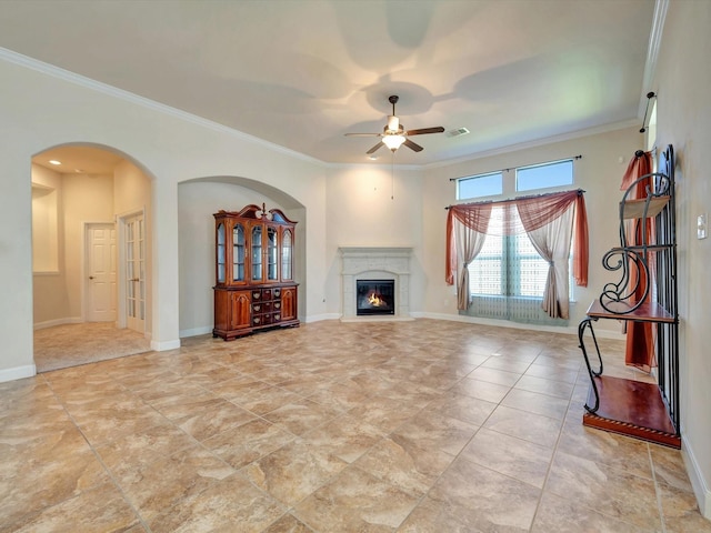 unfurnished living room featuring ornamental molding, ceiling fan, arched walkways, a high end fireplace, and baseboards