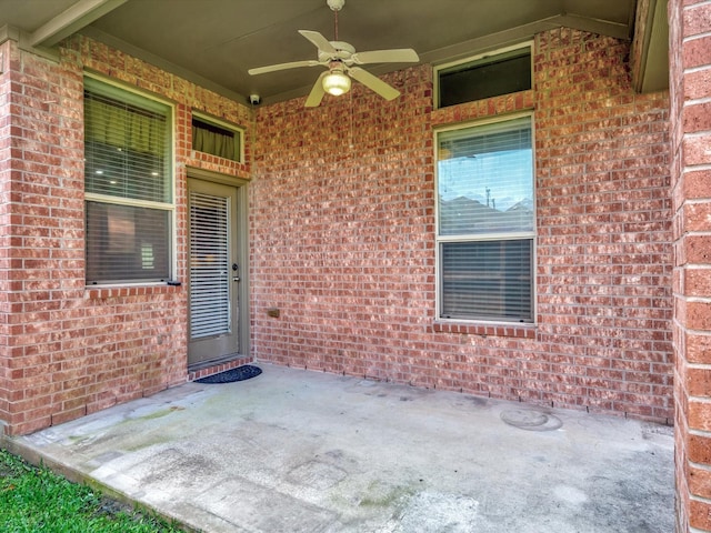 view of exterior entry with ceiling fan, a patio area, and brick siding