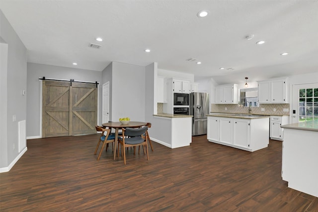 kitchen featuring black microwave, stainless steel fridge with ice dispenser, a barn door, dark wood finished floors, and tasteful backsplash