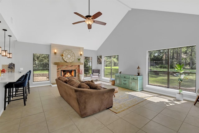 living room with high vaulted ceiling, light tile patterned floors, ceiling fan, a brick fireplace, and baseboards
