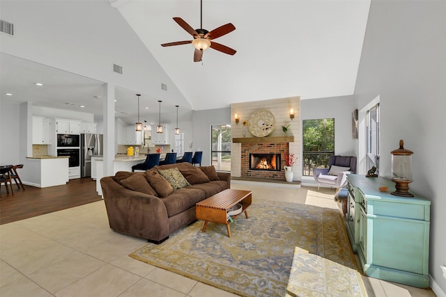 living room with high vaulted ceiling, a ceiling fan, light tile patterned floors, and a brick fireplace