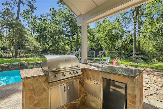 view of patio with area for grilling, a sink, a fenced backyard, exterior kitchen, and view of wooded area