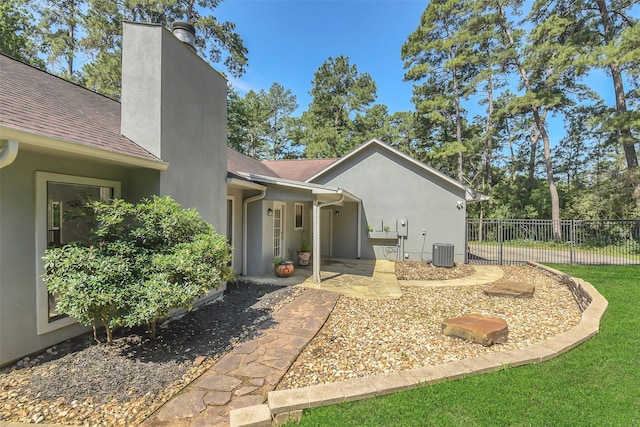 view of side of home with central air condition unit, fence, stucco siding, a chimney, and a shingled roof