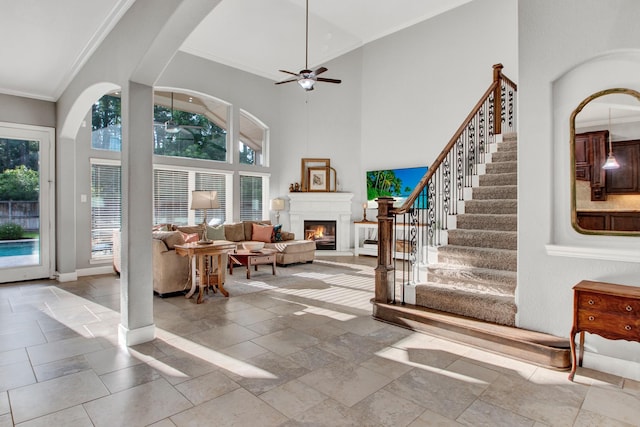 514 Chirping Sparrow Ct, Pinehurst, TX 77362 - living area featuring a ceiling fan, a glass covered fireplace, crown molding, stairway, and a towering ceiling