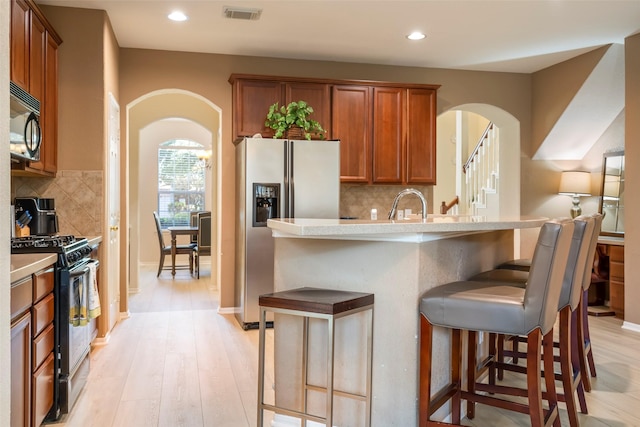 21623 Balsam Brook Ln, Katy, TX 77450 - kitchen with gas range, stainless steel refrigerator with ice dispenser, black microwave, arched walkways, and tasteful backsplash