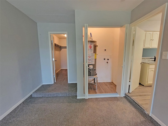 unfurnished bedroom featuring water heater, light colored carpet, a spacious closet, a closet, and baseboards