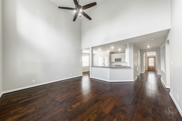 3722 Rocky Ledge Ln, Katy, TX 77494 - unfurnished living room featuring arched walkways, a ceiling fan, dark wood-style floors, a towering ceiling, and baseboards
