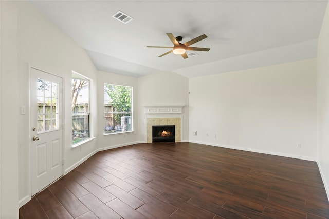 unfurnished living room with a ceiling fan, vaulted ceiling, dark wood-style floors, a tiled fireplace, and baseboards