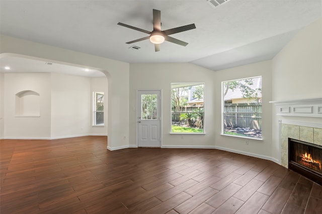 unfurnished living room featuring a fireplace, dark wood finished floors, ceiling fan, arched walkways, and baseboards