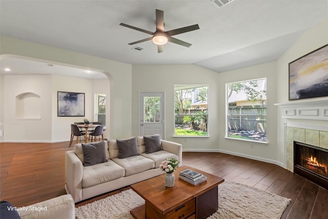 living area with wood finished floors, arched walkways, a ceiling fan, a tiled fireplace, and baseboards