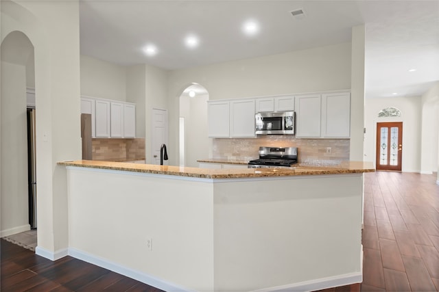 kitchen with appliances with stainless steel finishes, arched walkways, dark wood finished floors, light stone countertops, and white cabinets