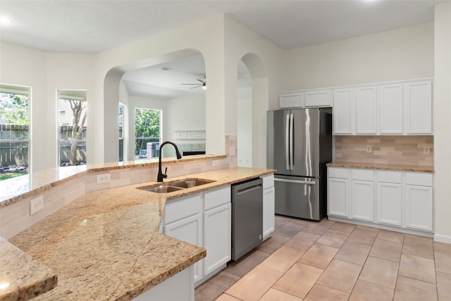 kitchen featuring stainless steel appliances, a sink, arched walkways, ceiling fan, and decorative backsplash