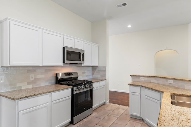 kitchen featuring stainless steel appliances, backsplash, white cabinets, recessed lighting, and light stone countertops