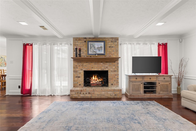living area featuring a textured ceiling, dark wood-style floors, beamed ceiling, a fireplace, and crown molding