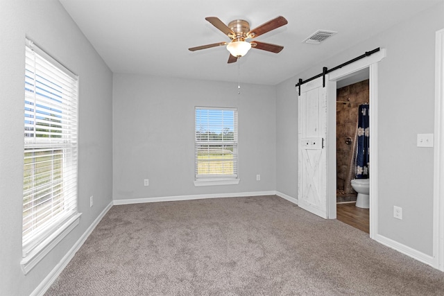 1107 Cypress St, Diboll, TX 75941 - unfurnished bedroom featuring carpet floors, a barn door, baseboards, ensuite bathroom, and a ceiling fan
