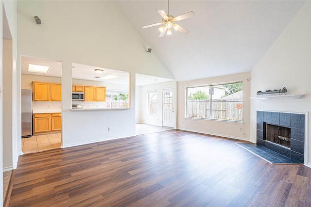 unfurnished living room with wood finished floors, a fireplace, high vaulted ceiling, a ceiling fan, and baseboards