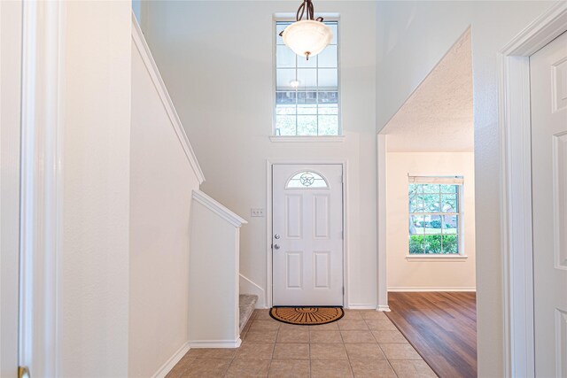 tiled foyer with stairs, a high ceiling, and baseboards