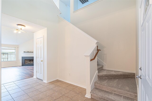 staircase featuring tile patterned flooring, baseboards, a fireplace, and a ceiling fan
