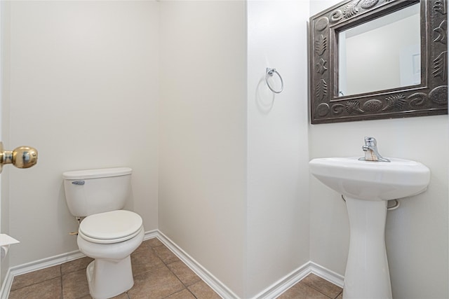 half bathroom featuring toilet, tile patterned flooring, baseboards, and a sink