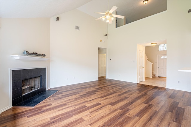 unfurnished living room with a ceiling fan, wood finished floors, a tile fireplace, high vaulted ceiling, and baseboards