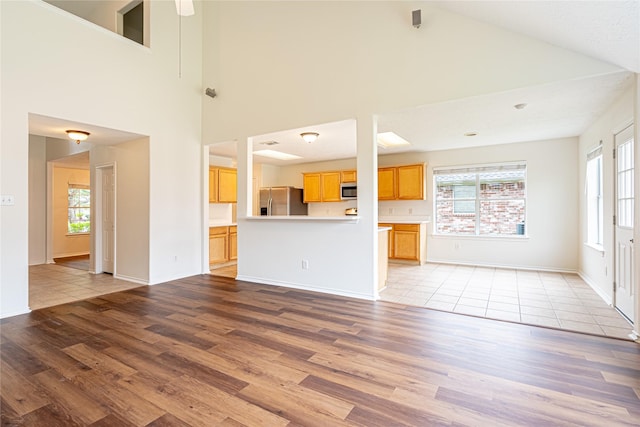 unfurnished living room featuring high vaulted ceiling, light wood finished floors, plenty of natural light, and baseboards