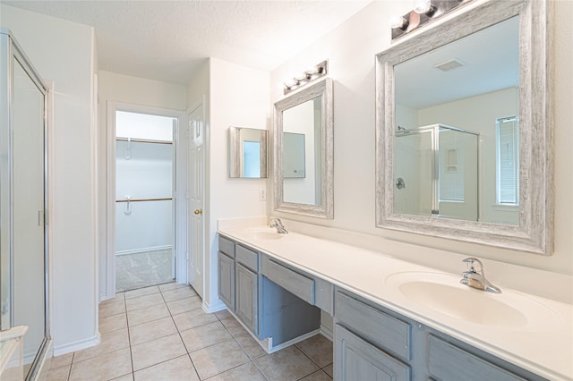 bathroom featuring a stall shower, tile patterned flooring, double vanity, a spacious closet, and a textured ceiling