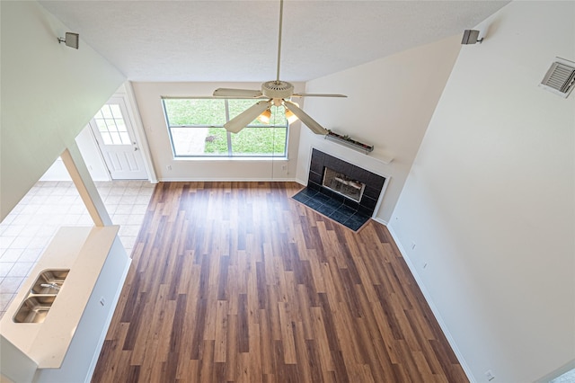 unfurnished living room featuring ceiling fan, baseboards, wood finished floors, a fireplace, and a textured ceiling