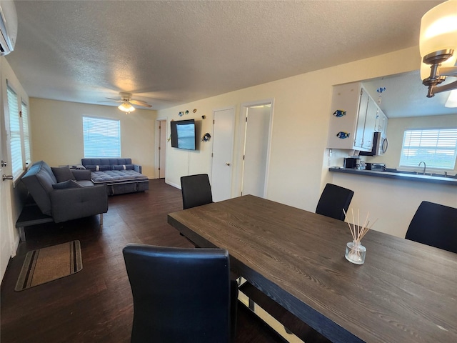 dining room featuring a textured ceiling, dark wood finished floors, healthy amount of natural light, a ceiling fan, and an AC wall unit