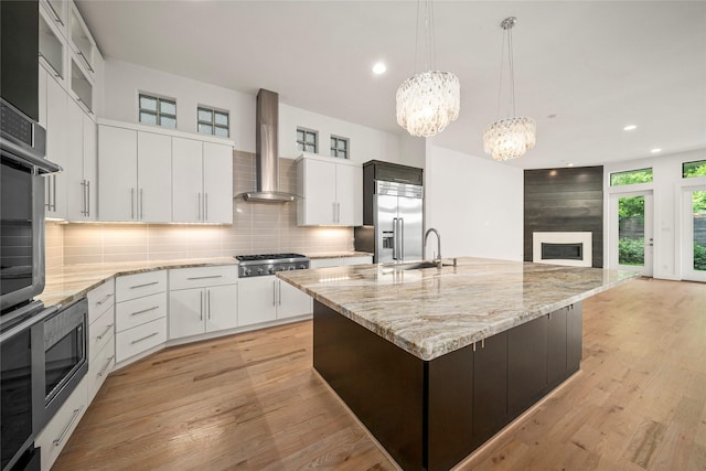 kitchen featuring wall chimney exhaust hood, appliances with stainless steel finishes, a chandelier, decorative backsplash, and a sink
