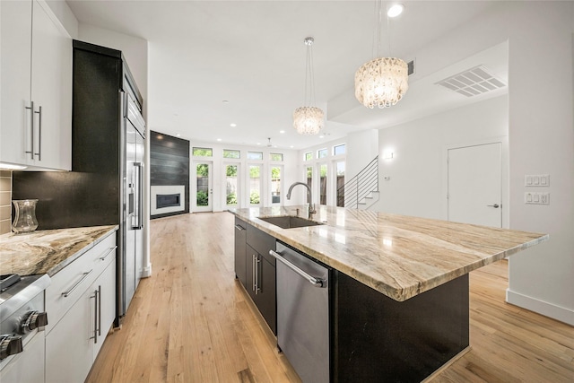 kitchen with a sink, stainless steel dishwasher, recessed lighting, light wood-type flooring, and light stone counters