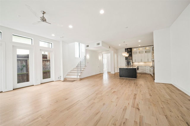 unfurnished living room featuring light wood-style flooring, stairs, ceiling fan, recessed lighting, and baseboards