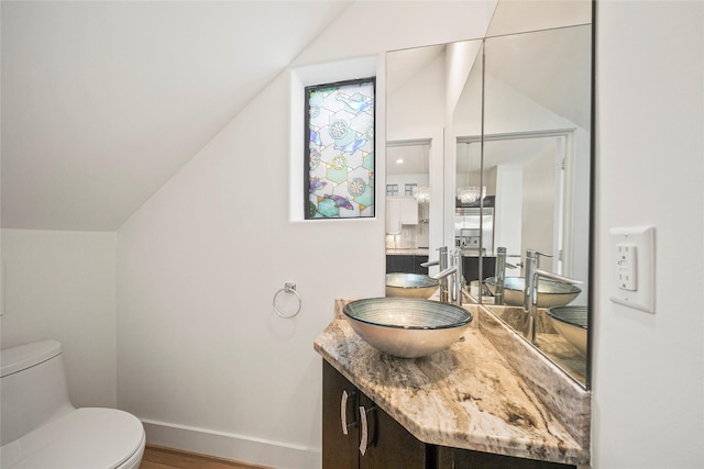 bathroom featuring vaulted ceiling, toilet, vanity, baseboards, and wood finished floors