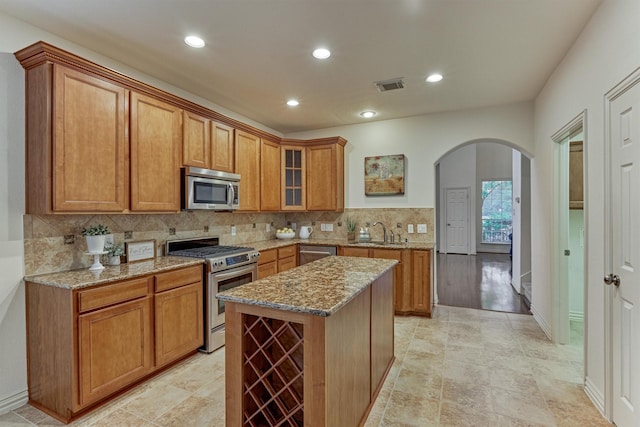 71 Ginger Jar St, The Woodlands, TX 77382 - kitchen with stainless steel appliances, arched walkways, a sink, brown cabinets, and tasteful backsplash