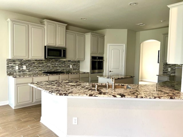 4923 Lacebark Pine Trl, Rosenberg, TX 77471 - kitchen with stainless steel appliances, a sink, arched walkways, decorative backsplash, and light stone counters