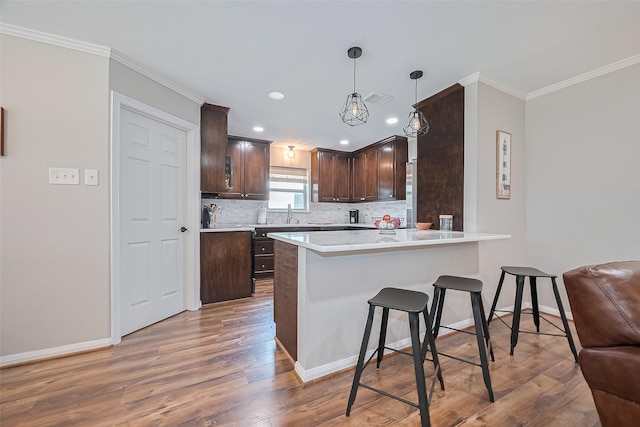 kitchen featuring dark brown cabinetry, light wood-style flooring, a breakfast bar area, decorative backsplash, and ornamental molding