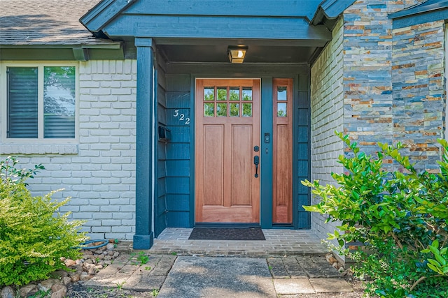 entrance to property featuring brick siding and roof with shingles