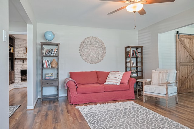 living room featuring a barn door, ceiling fan, wood finished floors, and a brick fireplace