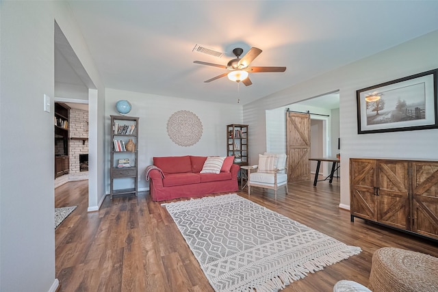 living area featuring a barn door, ceiling fan, a brick fireplace, and wood finished floors