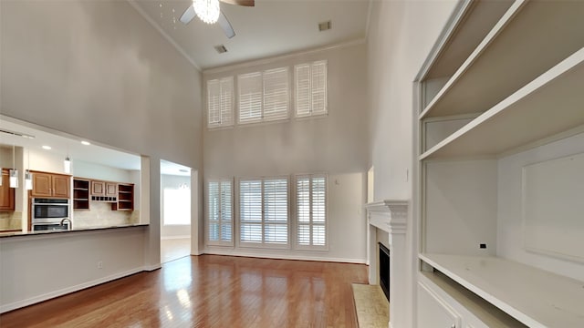 11111 Monte Rosa Ct, Richmond, TX 77406 - unfurnished living room featuring ornamental molding, a ceiling fan, a fireplace with flush hearth, high vaulted ceiling, and wood finished floors