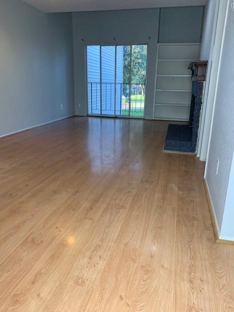 spare room with wood finished floors, a brick fireplace, and baseboards