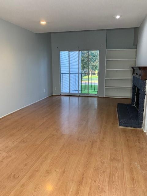 unfurnished living room with a fireplace, wood finished floors, baseboards, and recessed lighting