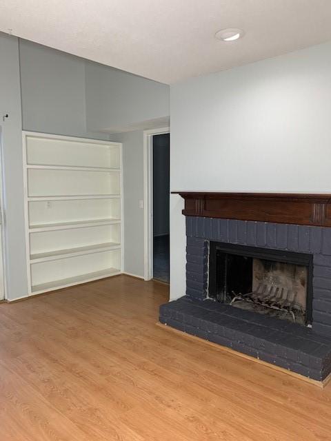 unfurnished living room with a brick fireplace, wood finished floors, and built in features